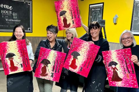 a group of women holding up paintings in front of a yellow wall