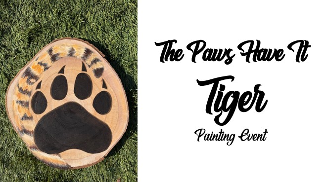 A wooden slice painted with a black paw print and tiger stripes, displayed beside the text "The Paws Have It Tiger Painting Event," captures the playful spirit of this unique tiger painting event.