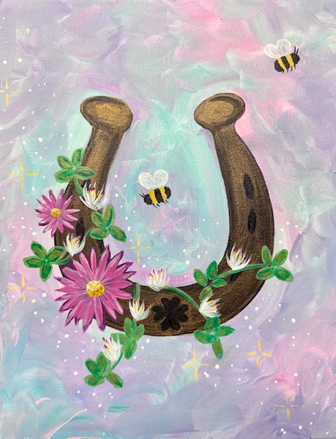 A horseshoe surrounded by pink and white flowers, with two bees from "Deez Lucky Beez" buzzing nearby, is set against a pastel-colored background, capturing the whimsical charm of a painting event.