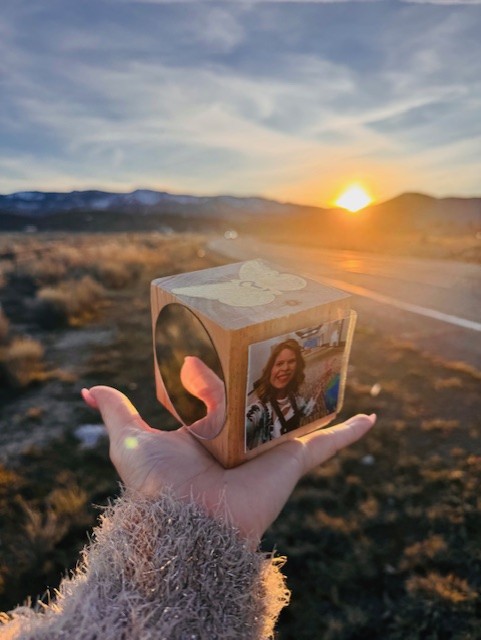 You Cube ~A Self-Discovery & Personal Growth Project 3 A hand holds a wooden photo cube with a woman's picture on one side, set against a sunset landscape with mountains in the background.