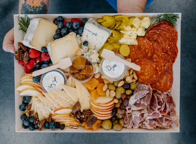 A platter reminiscent of a painting event masterpiece, boasting assorted cheeses, sliced meats, olives, nuts, sliced apples, berries, pickles, and chutneys—all arranged as if water under the bridge never disturbed this harmonious spread.